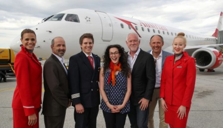 Sieben Personen posieren und lächeln vor einem Flugzeug der Austrian Airlines auf einer Flughafenpiste.