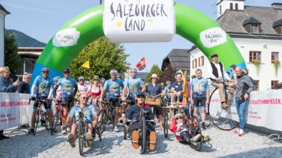 Radfahrer und Handbiker posieren unter einem grünen Bogen im Salzburger Land bei einer Freiluftveranstaltung.
