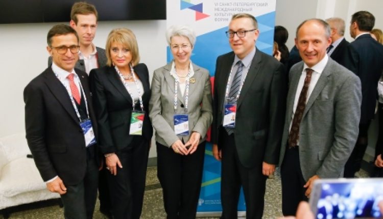 Sechs Personen in Geschäftskleidung posieren und lächeln für ein Gruppenfoto bei einer Konferenzveranstaltung.