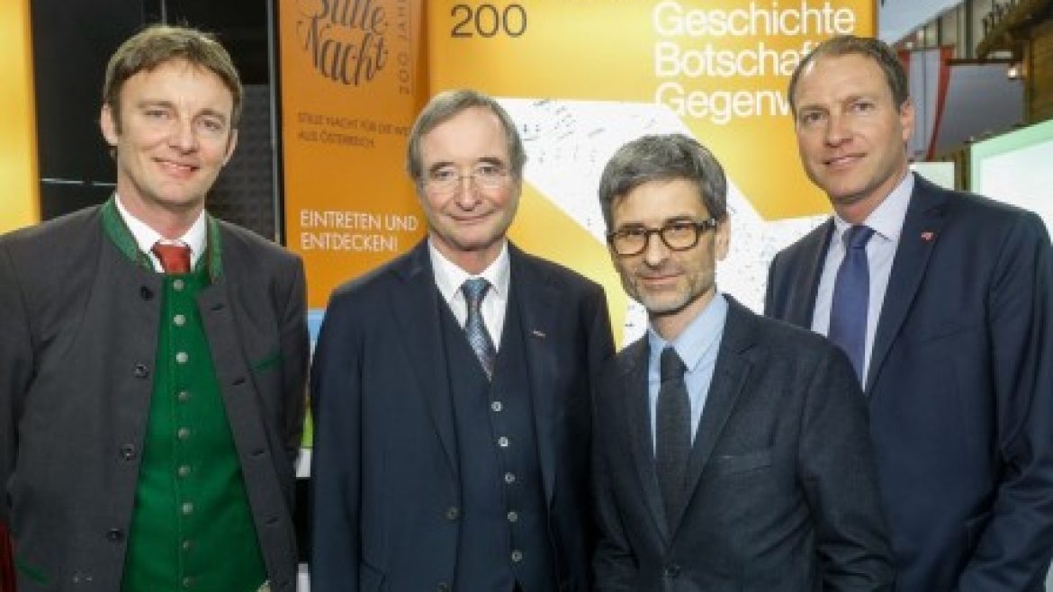 Vier Männer in Anzügen stehen lächelnd vor einer Ausstellung der Stillen Nacht 200.
