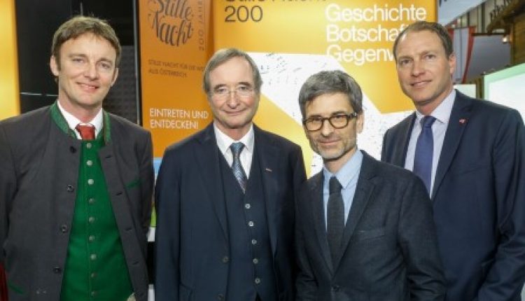 Vier Männer in Anzügen stehen lächelnd vor einer Ausstellung der Stillen Nacht 200.