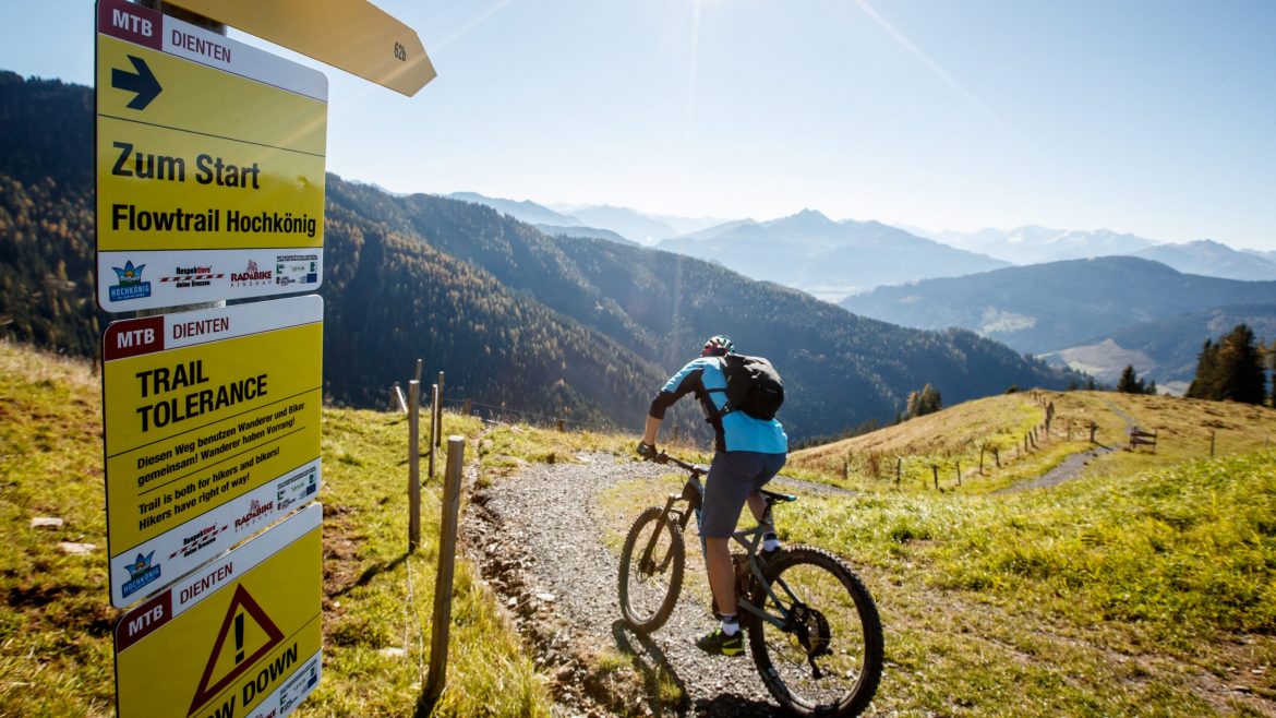 Ein Mountainbike-Fahrer fährt auf einer landschaftlich reizvollen Strecke in der Nähe eines Hinweisschildes, umgeben von Hügeln und Bergen.