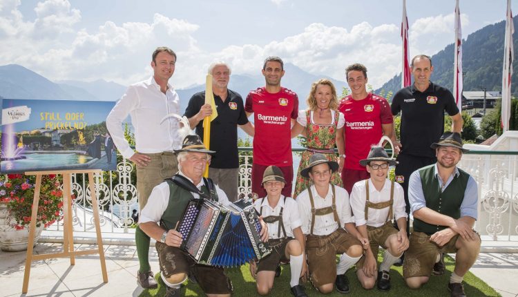 Eine Gruppe von Menschen in traditioneller österreichischer Kleidung und Fußballtrikots posiert im Freien mit Bergen im Hintergrund.