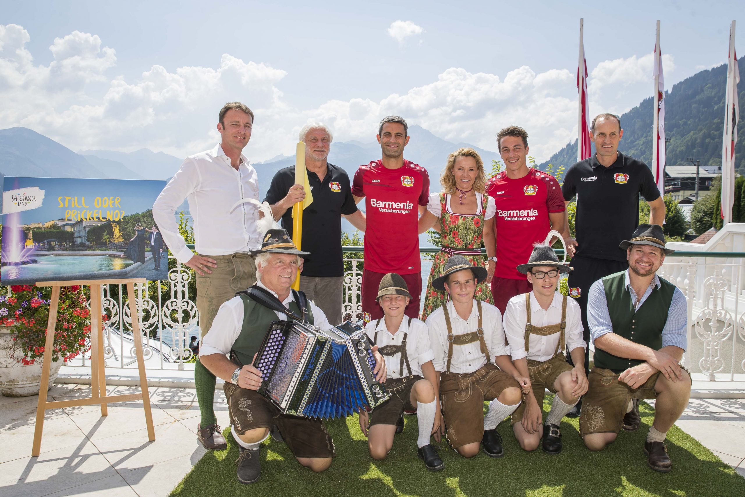 Eine Gruppe von Menschen in traditioneller österreichischer Kleidung und Fußballtrikots posiert im Freien mit Bergen im Hintergrund.