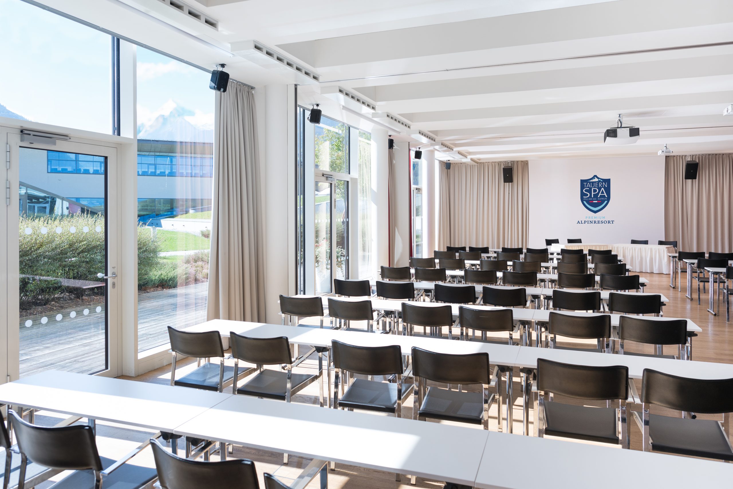Heller Konferenzraum mit Stuhlreihen, Tischen, großen Fenstern und einem SPA ACADEMY-Schild an der Stirnseite.