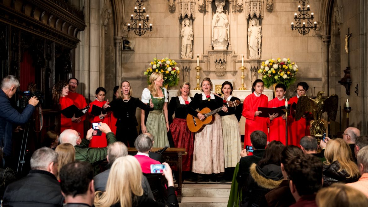 Ein Chor singt in einer Kirche; eine Frau spielt Gitarre, während das Publikum zusieht und Fotos macht.
