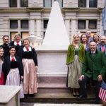 Eine Gruppe von Menschen in traditioneller Kleidung posiert vor dem Grab von Alexander Hamilton auf einem städtischen Friedhof.
