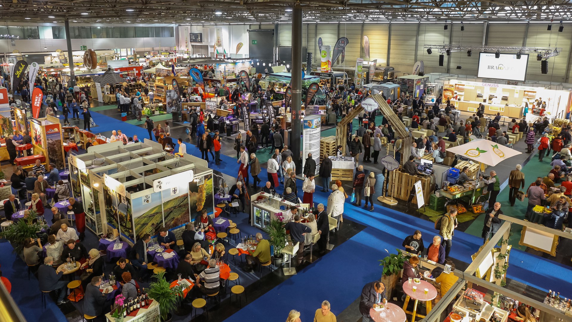 Eine geschäftige Messe oder Ausstellung mit vielen Ständen, Auslagen und Menschen, die herumlaufen, sitzen und sich unterhalten.