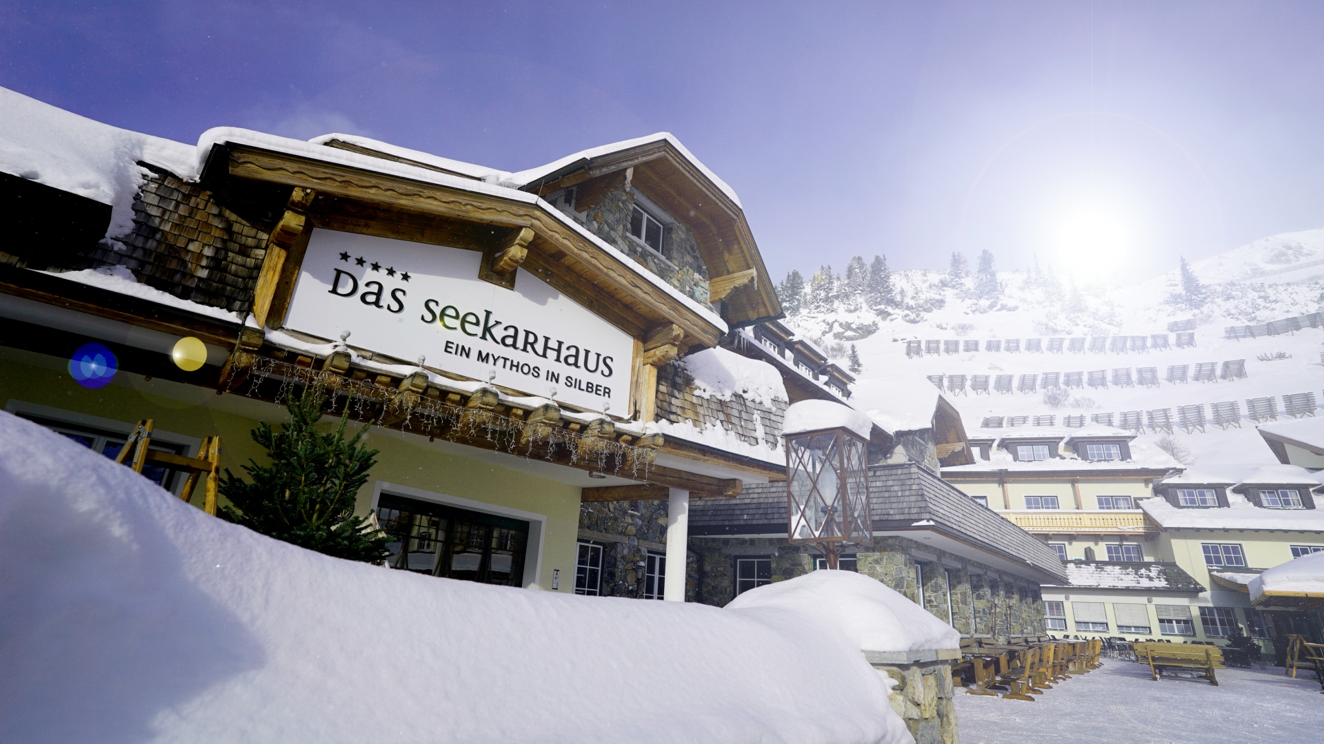 Ein verschneites Alpenhotel mit dem Schild "Das Seekarhaus" unter einem strahlend sonnigen Winterhimmel.