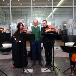 Ein Streichquartett tritt auf, und zwischen den Geigern steht ein lächelnder Mann in einer grünen Weste.