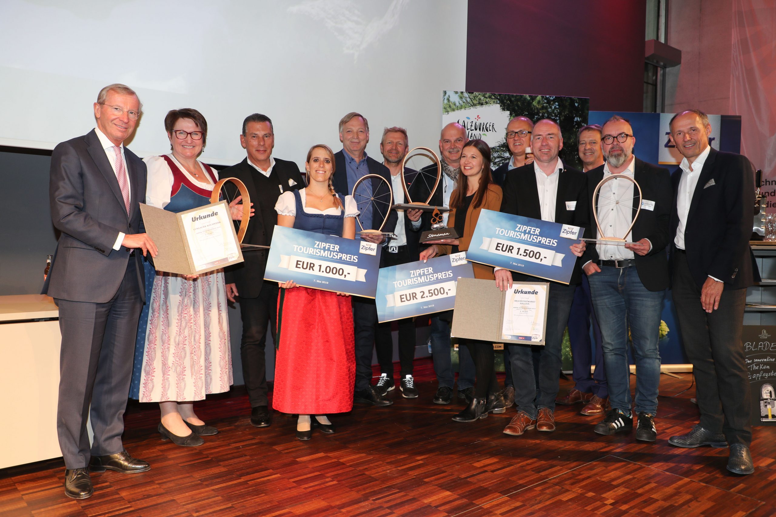 Eine Gruppe von Personen posiert mit Preisschecks und Urkunden bei einer Preisverleihung in einem Innenraum.