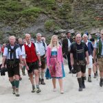 Eine Gruppe von Menschen in traditioneller österreichischer Kleidung geht im Freien auf einem unbefestigten Weg in den Bergen.