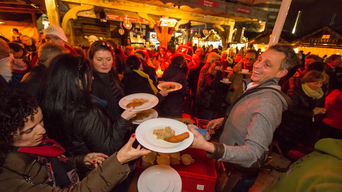 Menschen versammeln sich an einem belebten Essensstand und nehmen auf einem lebhaften Nachtmarkt im Freien Teller mit Essen entgegen.