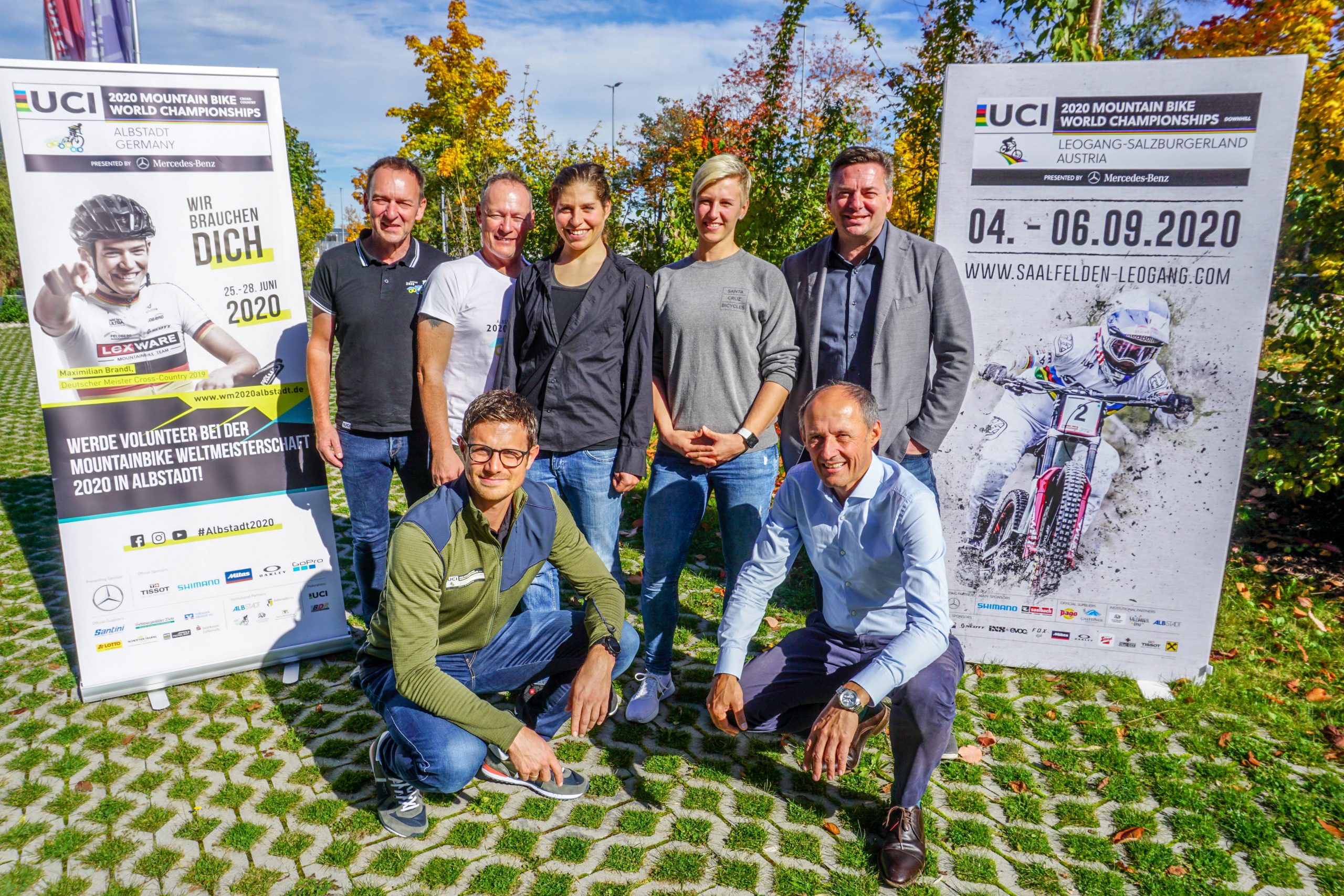Sieben Personen posieren im Freien zwischen zwei Plakaten für die UCI Mountainbike-Weltmeisterschaften 2020 in Leogang.