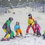 Ein Skilehrer bringt vier Kindern in einer großen Schneehalle das Skifahren bei.
