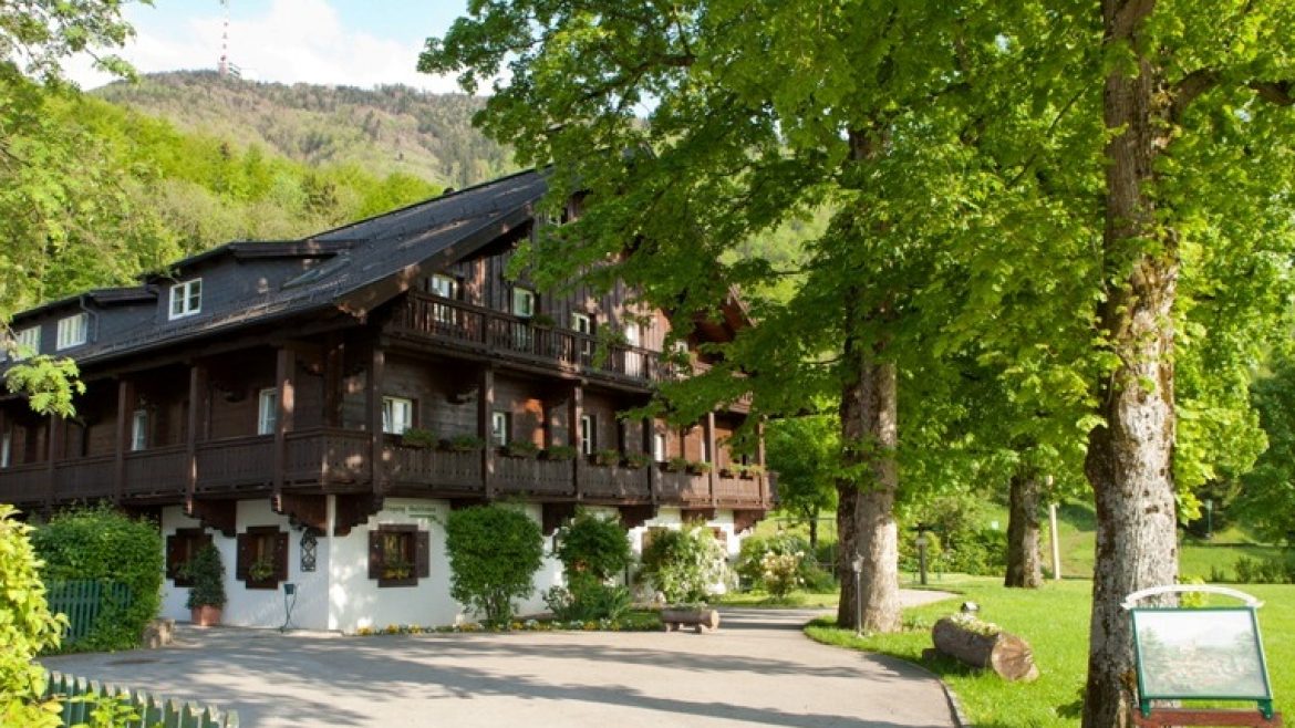 Ein traditionelles Holzhaus mit Balkonen, umgeben von üppig grünen Bäumen an einem sonnigen Tag.