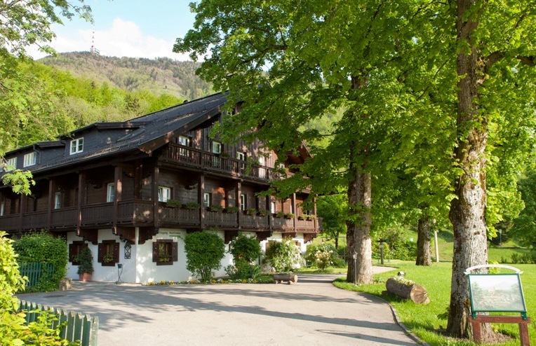 Ein traditionelles Holzhaus mit Balkonen, umgeben von üppig grünen Bäumen an einem sonnigen Tag.