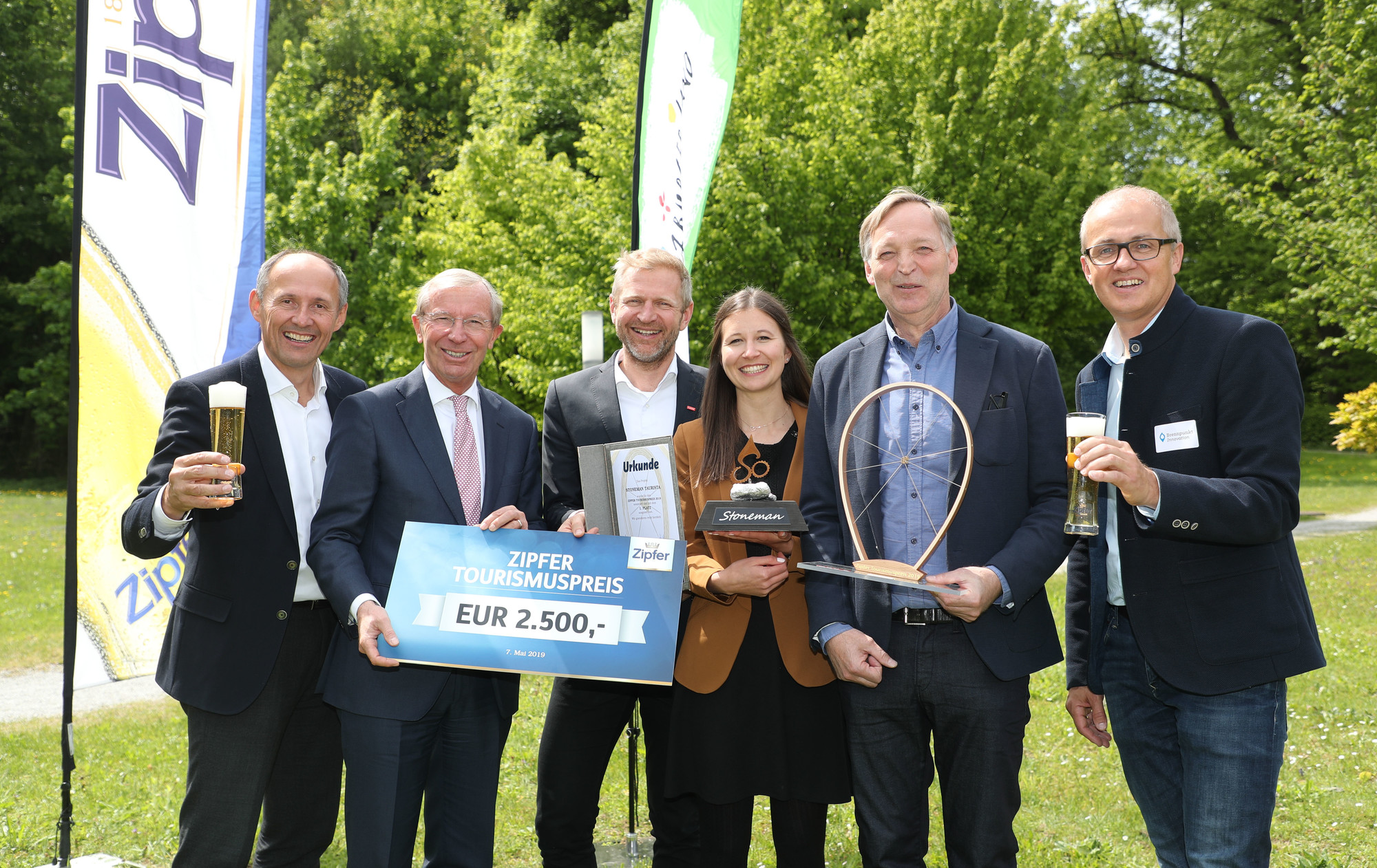 Sechs lächelnde Menschen halten eine Trophäe, ein Preisschild und Getränke bei einer Veranstaltung zur Verleihung des Outdoor-Tourismuspreises.