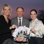 Drei Menschen lächeln und halten Lifestyle-Magazine im Freien bei Sonnenuntergang hoch.