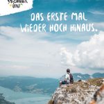 Ein Wanderer sitzt auf einem Berggipfel mit Blick auf Seen und Täler unter einem blauen, wolkenverhangenen Himmel.