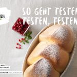 Draufsicht auf drei Brioche-Brötchen mit Puderzucker in einer Schale mit roten Johannisbeeren und Minze daneben auf einem weißen Tisch.