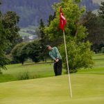 Ein Golfer in einem grünen Pullover chippt den Ball auf einem üppigen, malerischen Golfplatz ins Loch.