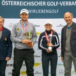 Vier Personen posieren bei einem Golfturnier; zwei halten Trophäen und tragen Medaillen, sie stehen vor einem Hintergrund mit Markenzeichen.