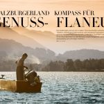 Ein Mann steht auf einem Holzboot auf einem See mit bewaldeten Hügeln und Bergen im Hintergrund bei Sonnenuntergang.