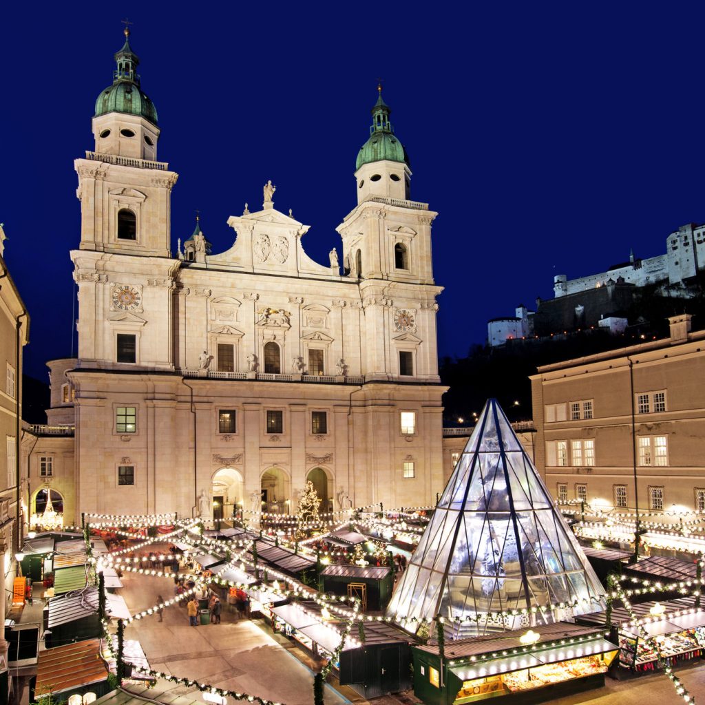 Salzburger Dom und Weihnachtsmarkt bei Nacht, mit festlicher Beleuchtung und einer Glaspyramide in der Mitte.