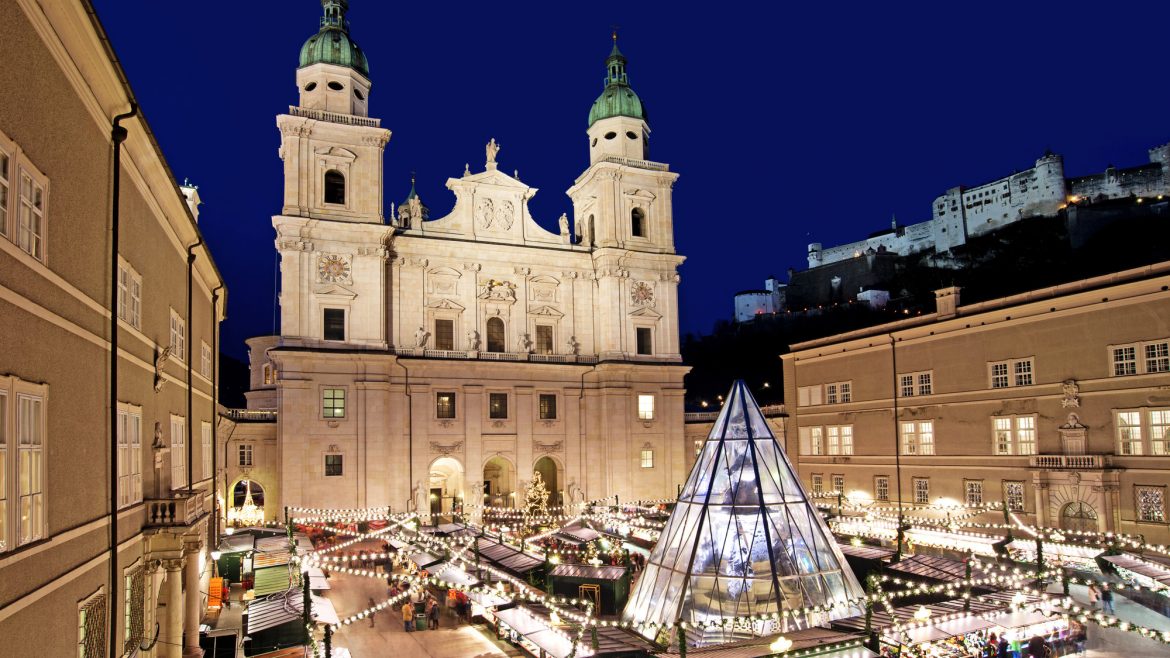 Salzburger Dom und Weihnachtsmarkt bei Nacht, mit festlicher Beleuchtung und einer Glaspyramide in der Mitte.