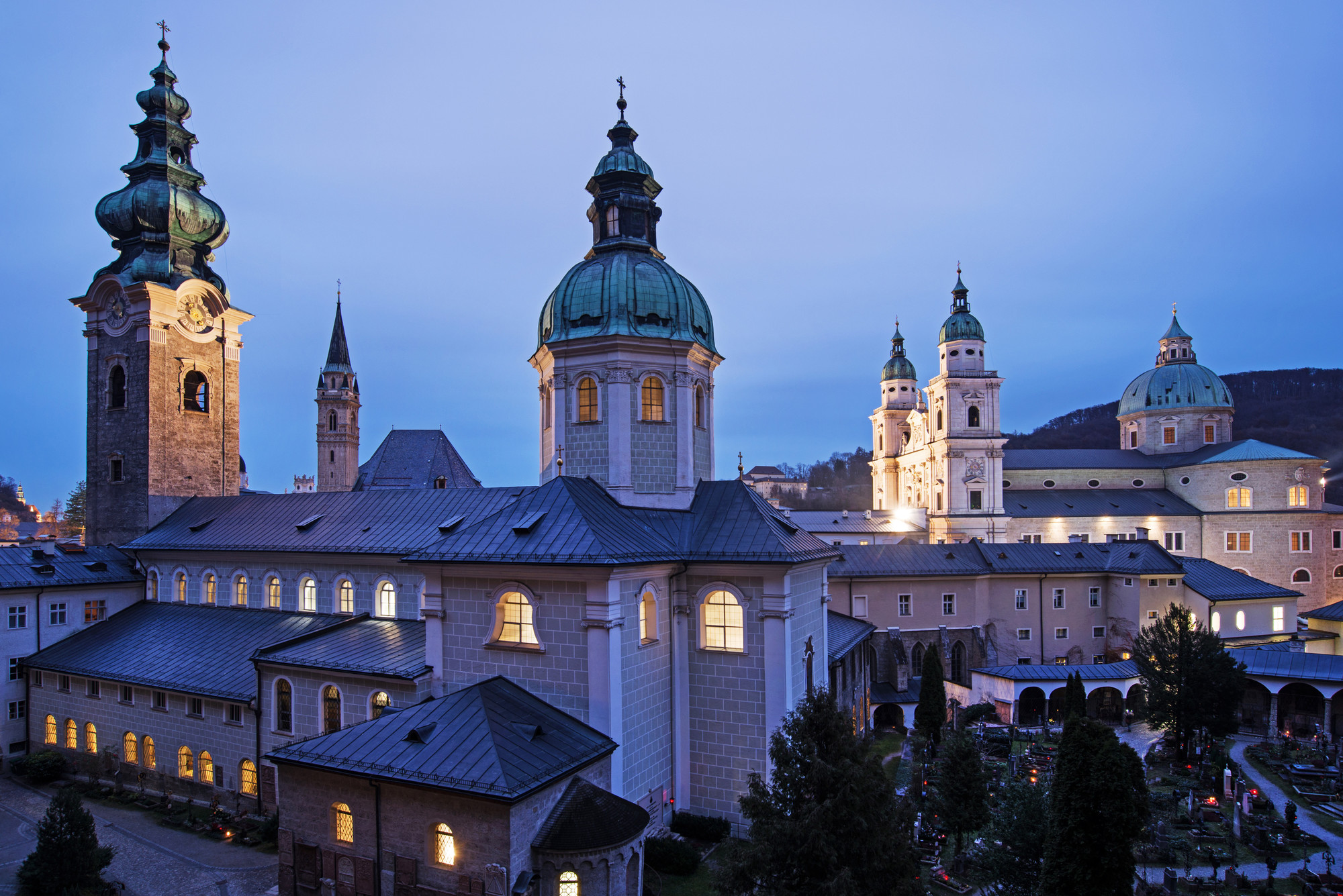 Historische Gebäude mit beleuchteten Kuppeln und Türmen in der Abenddämmerung in Salzburg, Österreich.