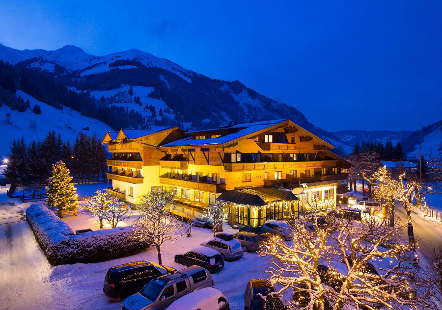 Ein hell erleuchtetes Berghotel, umgeben von Schnee und geschmückten Bäumen an einem Winterabend.