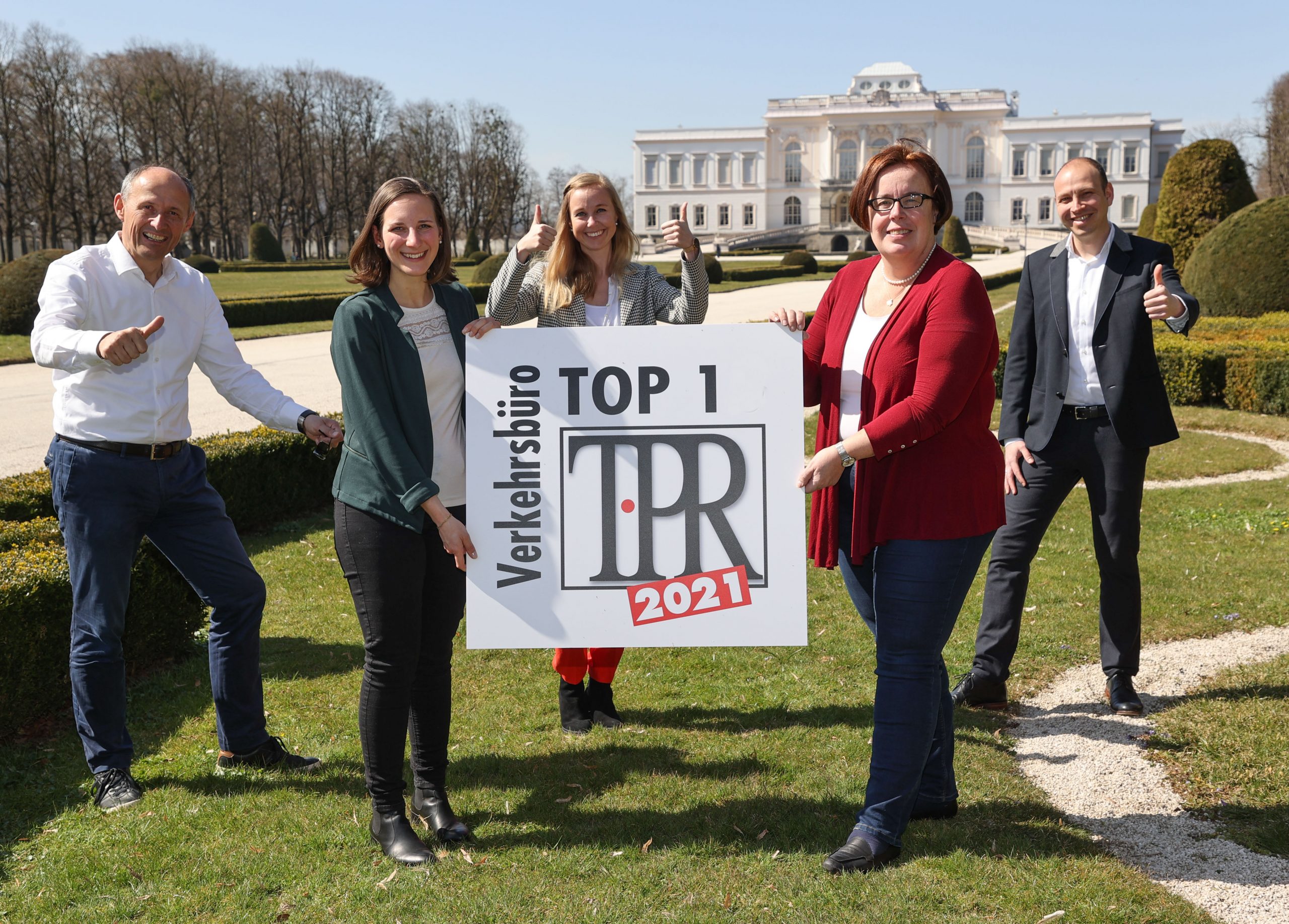 Fünf lächelnde Menschen im Freien, die ein Schild mit der Aufschrift TOP 1 Verkehrsbüro TPR 2021 halten und Daumen hoch zeigen.