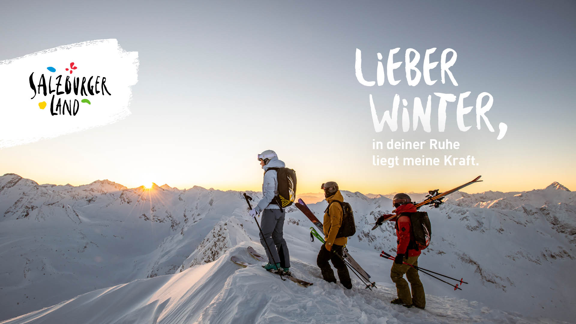 Drei Skifahrer stehen bei Sonnenaufgang auf einem verschneiten Berggipfel und bewundern die Winterlandschaft.