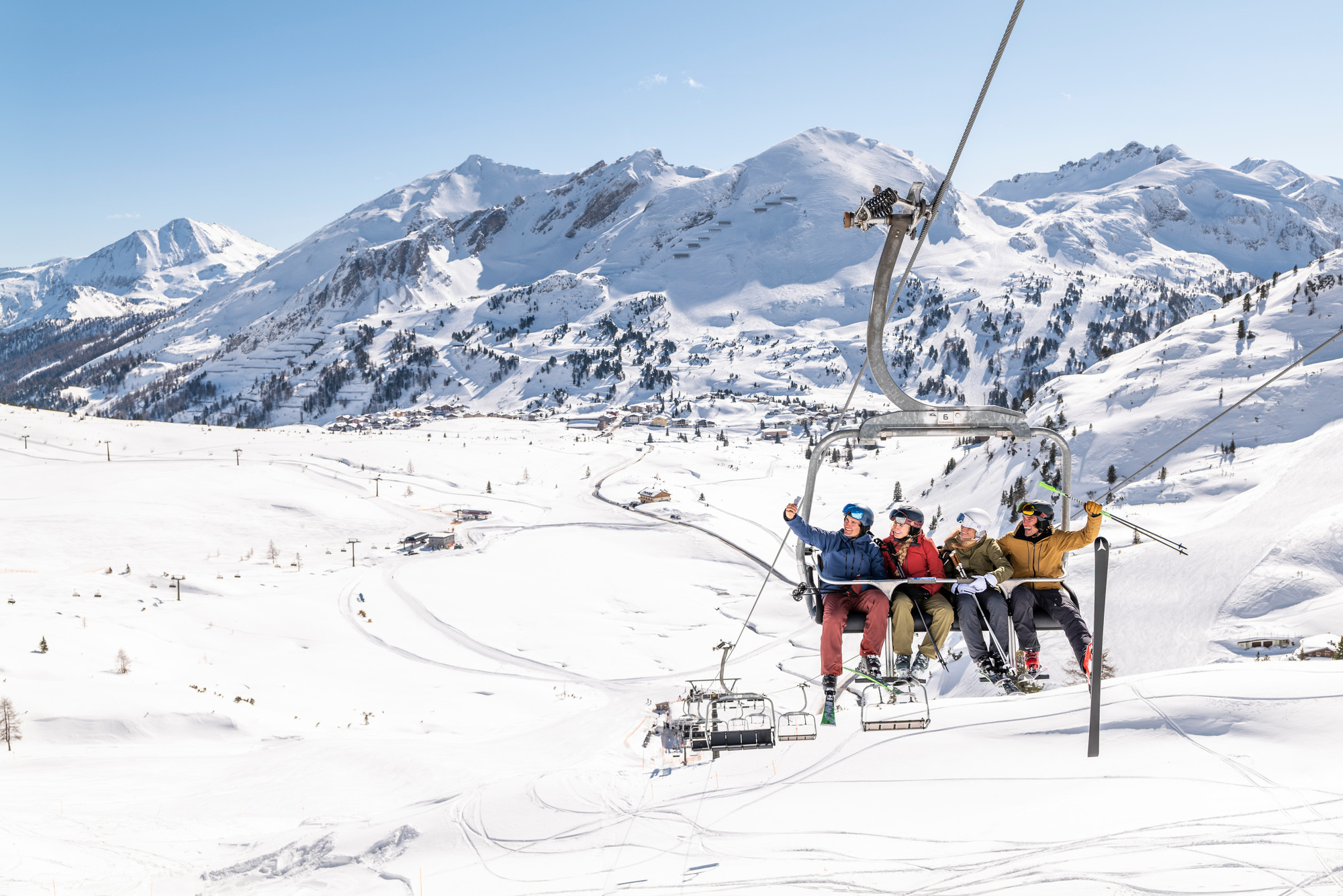 Vier Skifahrer fahren an einem hellen, klaren Tag mit einem Skilift über verschneite Berge.