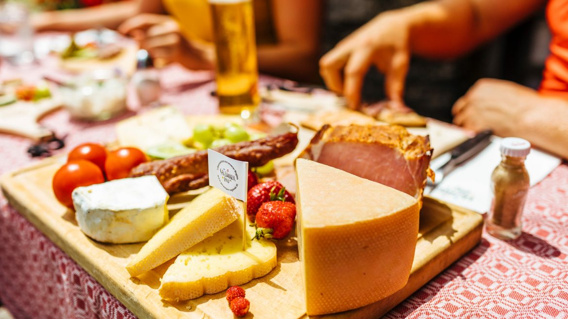 Ein Holzbrett mit verschiedenen Käsesorten, Wurstwaren, Tomaten und Erdbeeren auf einem Tisch im Freien.