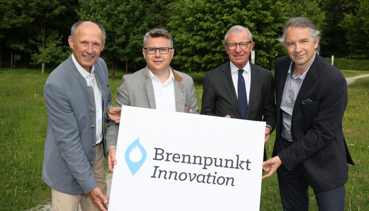 Vier Männer stehen im Freien und halten ein Schild mit der Aufschrift Brennpunkt Innovation und einem blauen Flammenlogo.