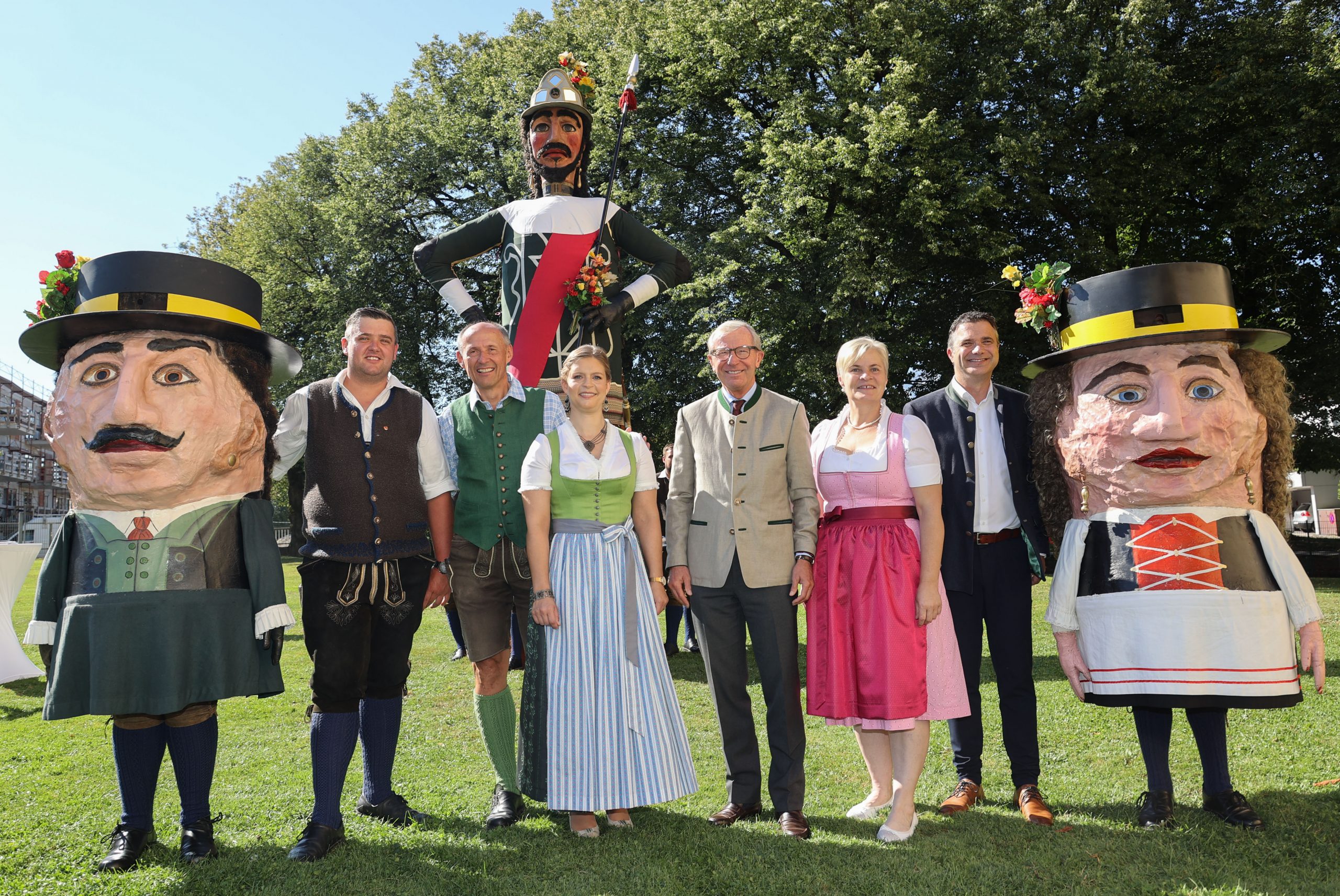 Acht Personen in traditioneller österreichischer Tracht stehen mit zwei großen Festspielpuppen und einer großen Soldatenfigur im Freien.