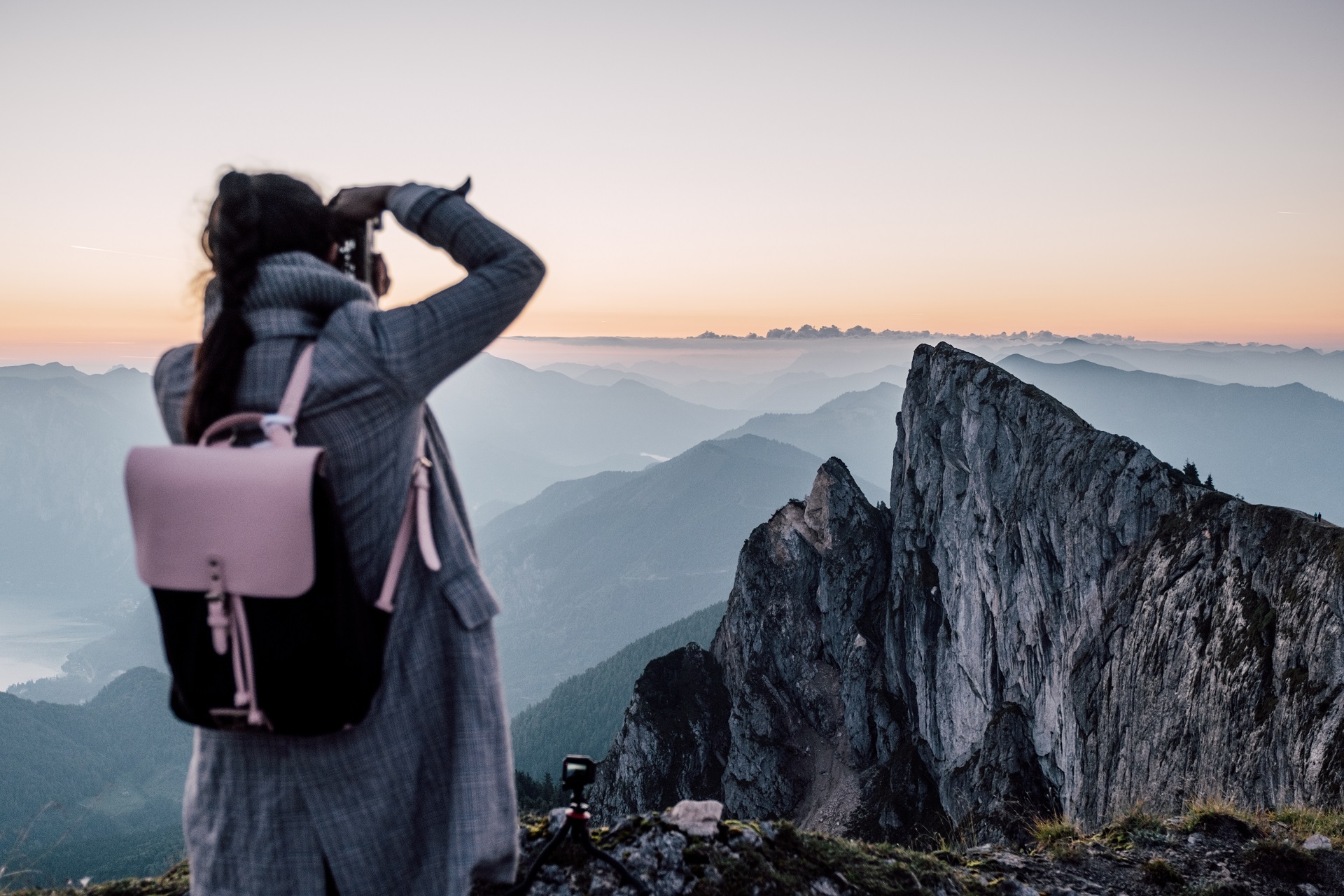 Person mit Rucksack, die ein Foto von zerklüfteten Berggipfeln bei Sonnenaufgang oder Sonnenuntergang macht.