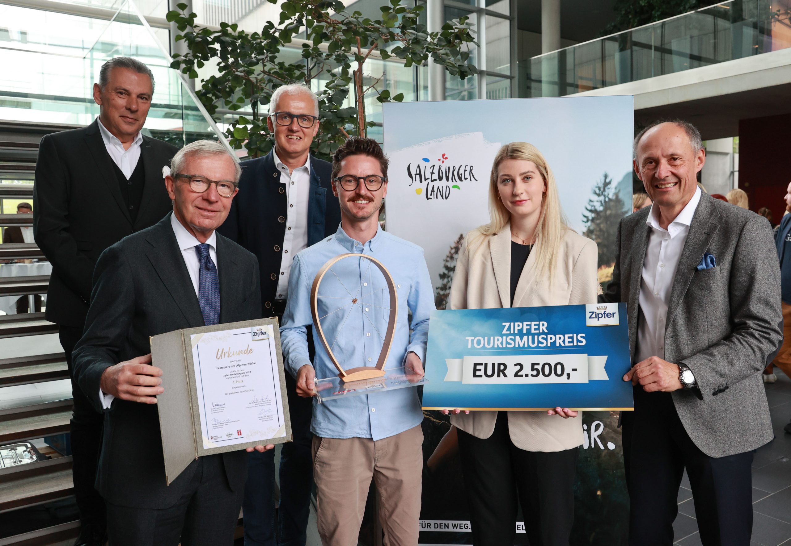 Sechs lächelnde Menschen in einem Raum, die eine Auszeichnung, eine Urkunde und ein Schild mit einem Tourismuspreis von 2 500 € in der Hand halten.