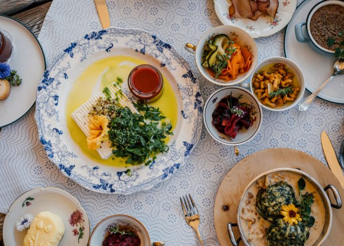 Ein Tisch mit verschiedenen bunten Gerichten, darunter Salate, Grünzeug, Soßen und Brot auf eleganten Tellern.