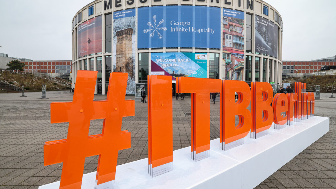 Großes orangefarbenes #ITBBerlin-Schild vor dem Gebäude der Messe Berlin mit darüber angebrachten Veranstaltungsbannern.