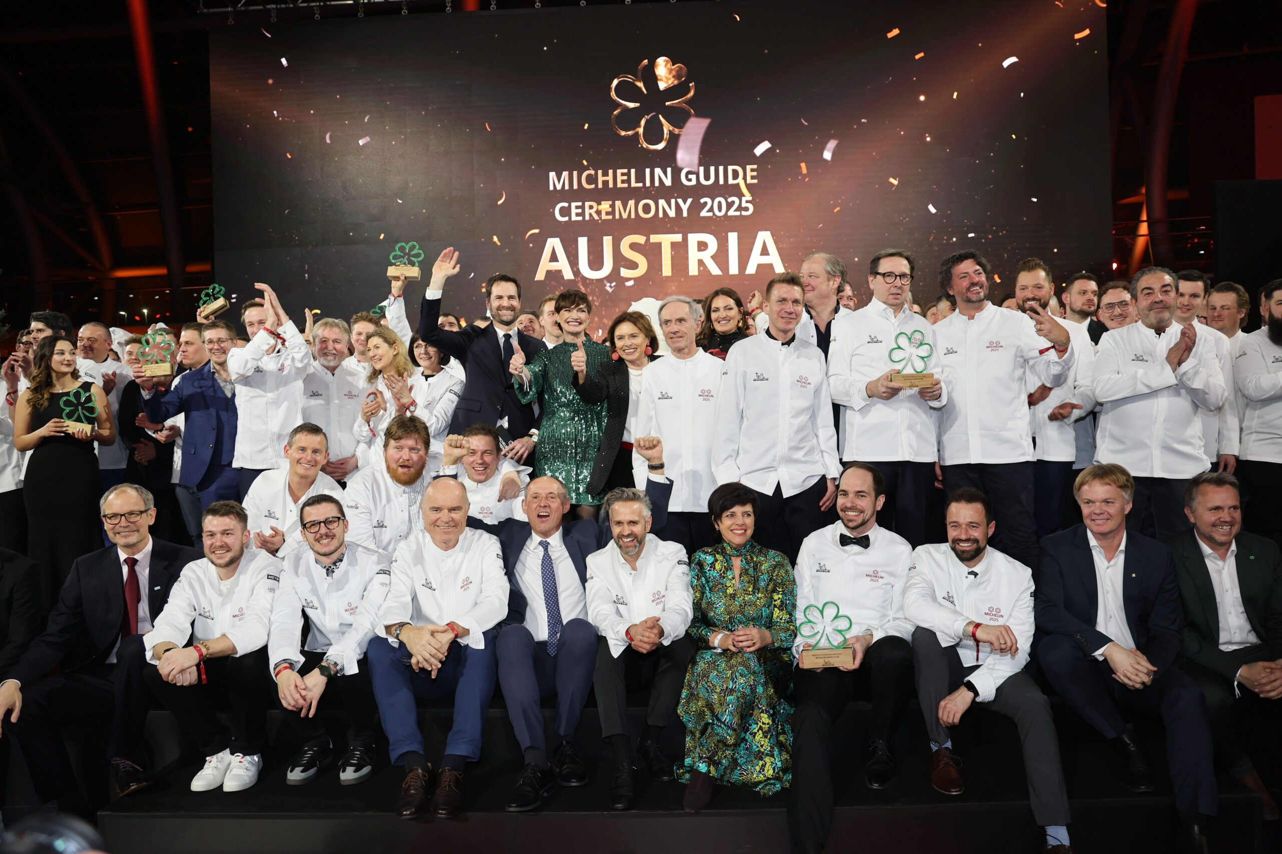 Eine große Gruppe von Köchen in weißen Jacken posiert auf der Bühne bei der Verleihung des Michelin-Führers Österreich 2025.