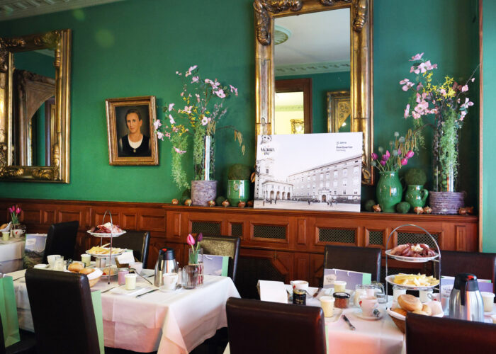 Elegantes Esszimmer mit grünen Wänden, Spiegeln, Blumen und gedeckten Tischen für das Frühstück mit verschiedenen Speisen.