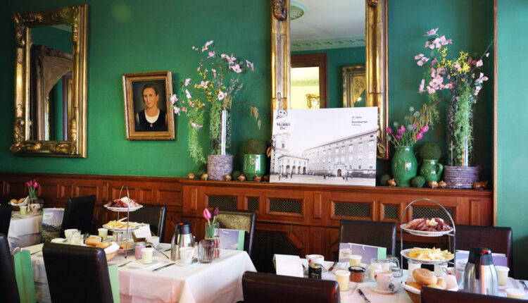 Elegantes Esszimmer mit grünen Wänden, Spiegeln, Blumen und gedeckten Tischen für das Frühstück mit verschiedenen Speisen.