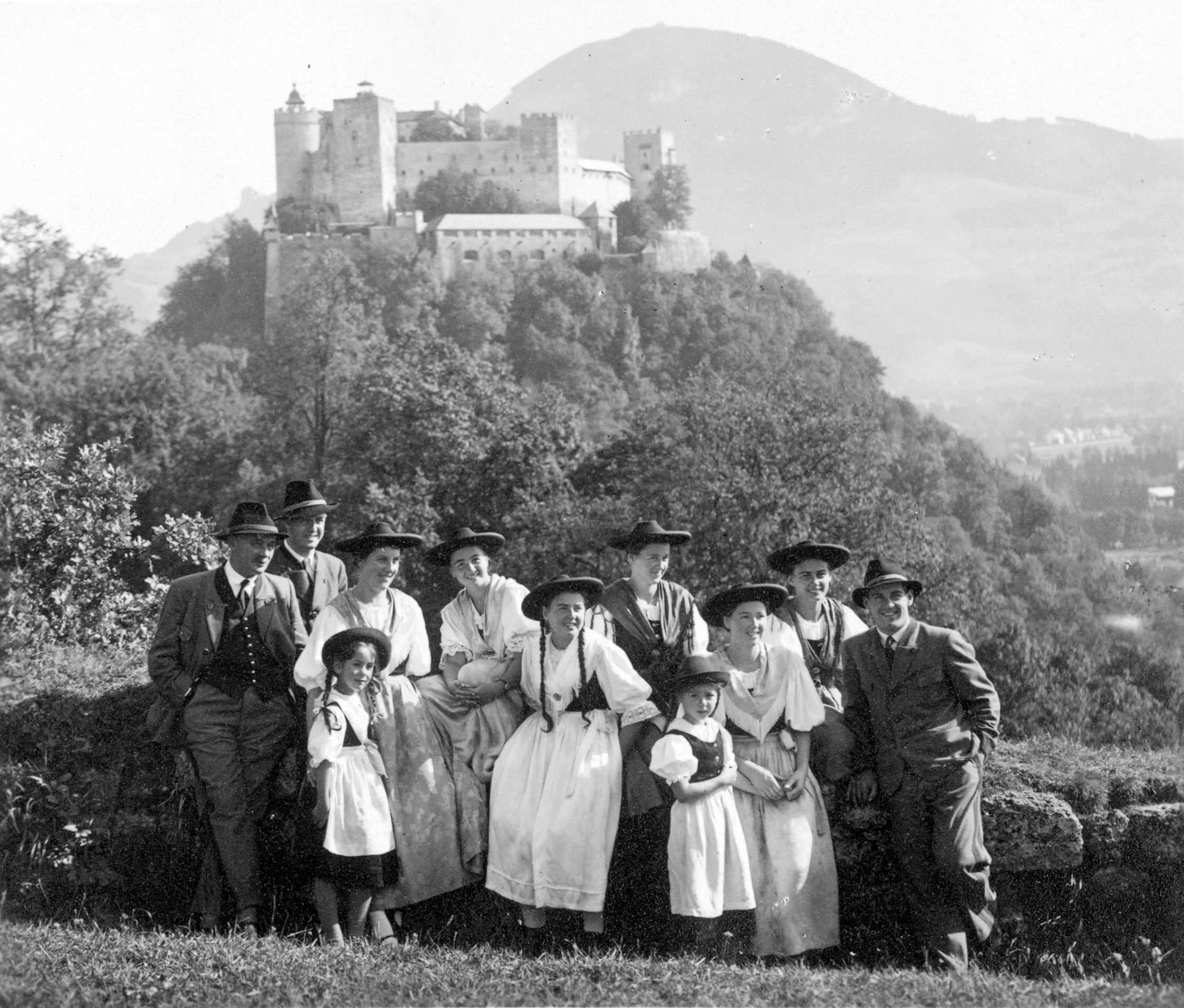 Eine Gruppe in traditioneller Kleidung posiert im Freien mit einer großen Burg auf einem Hügel im Hintergrund.