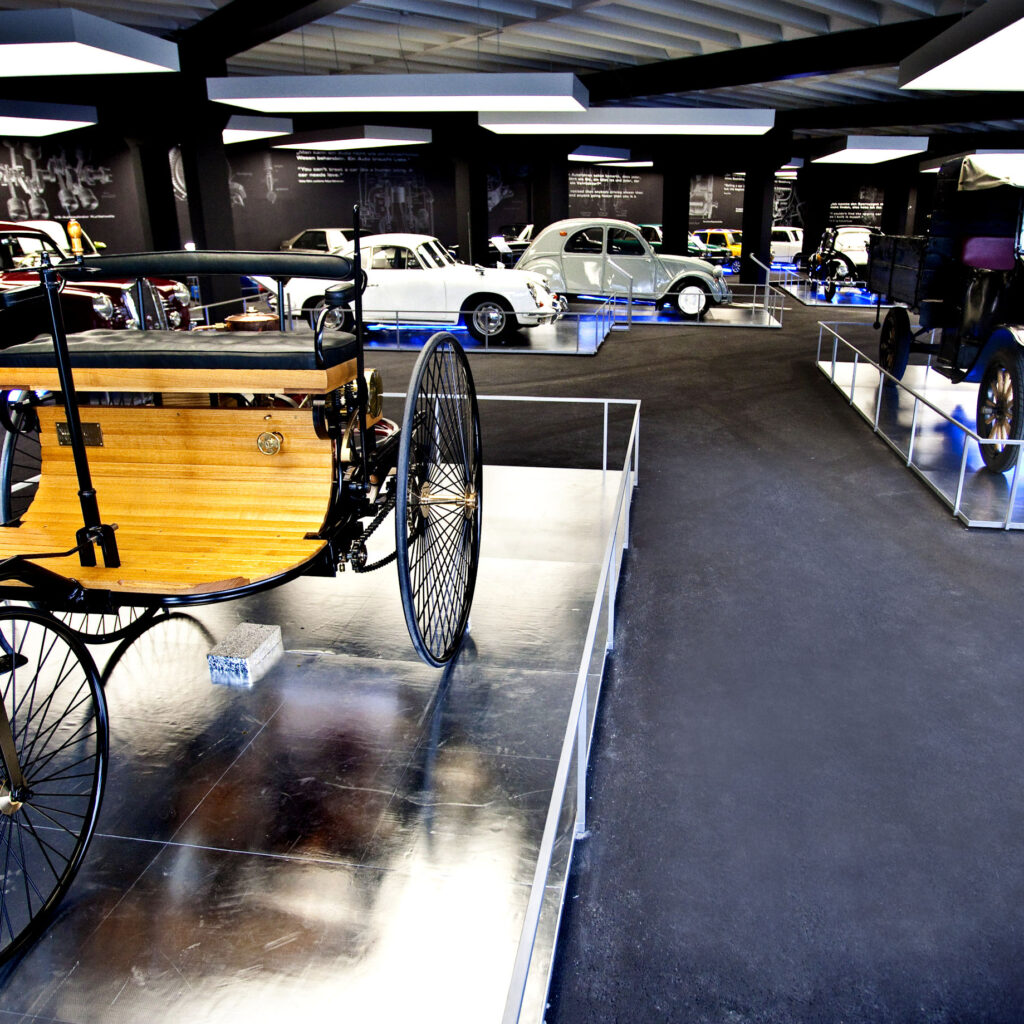 In einem Museum ausgestellte Oldtimer, mit einem hölzernen Oldtimer im Vordergrund.