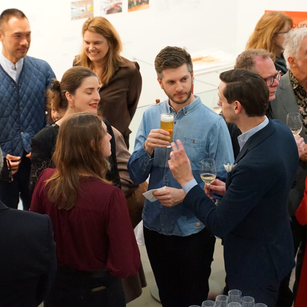 Eine Gruppe von Personen, die sich bei einer Veranstaltung in einem Gebäude oder bei einem Empfang mit Getränken trifft.