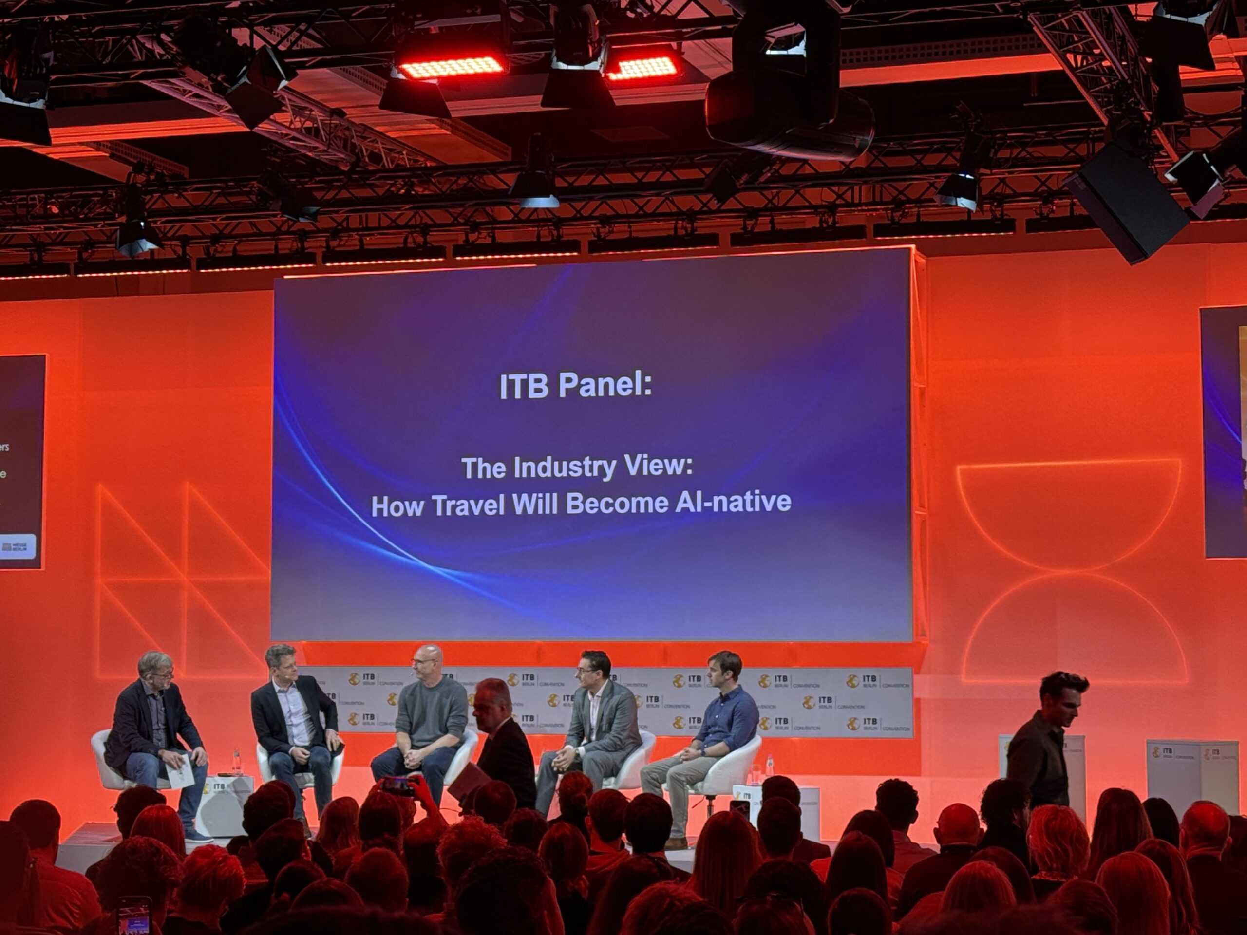 Fünf Diskussionsteilnehmer sitzen auf der Bühne und lesen auf einem Bildschirm: Wie Reisen auf dem ITB-Panel KI-nativ werden wird.