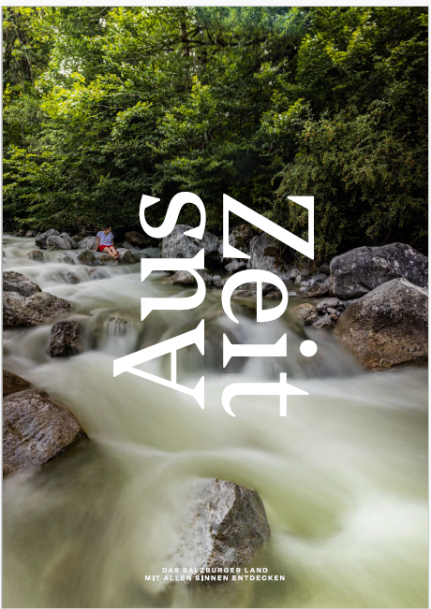 Ein Fluss fließt über Felsen in einem Wald; der Text Aus Zeit überlagert das Bild vertikal in großen weißen Buchstaben.